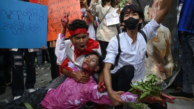 Next to an image of ousted civilian leader Aung San Suu Kyi, a protester covered in fake blood stages a performance representing the military’s killing of a nonviolent activist outside the UN office in Bangkok on February 1, the third anniversary of the coup in Myanmar. (Lillian Suwanrumpha/AFP)
