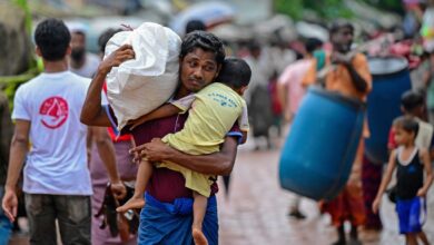 A Rohingya refugee holds his child while carrying relief supplies at a camp in Cox’s Bazar, Bangladesh (Photo: Munir Uz Zaman / AFP)