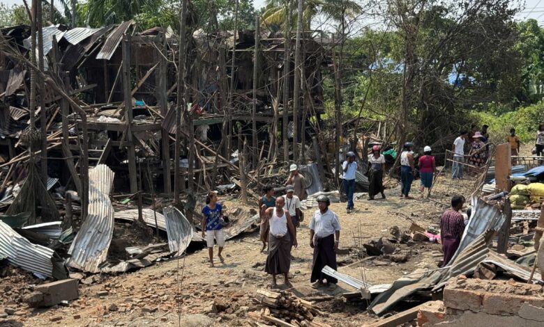 ယနေ့ မေ ၁၅ ရက်နေ့က ကျောက်တော်မြို့ ရွာမရပ်ကွက် ဗုံးကြဲခံရသည့် ထိခိုက်ပျက်စီးမှုများအနီး တွေ့ရသော ဒေသခံတချို့။ (ဓာတ်ပုံ -AFP)
