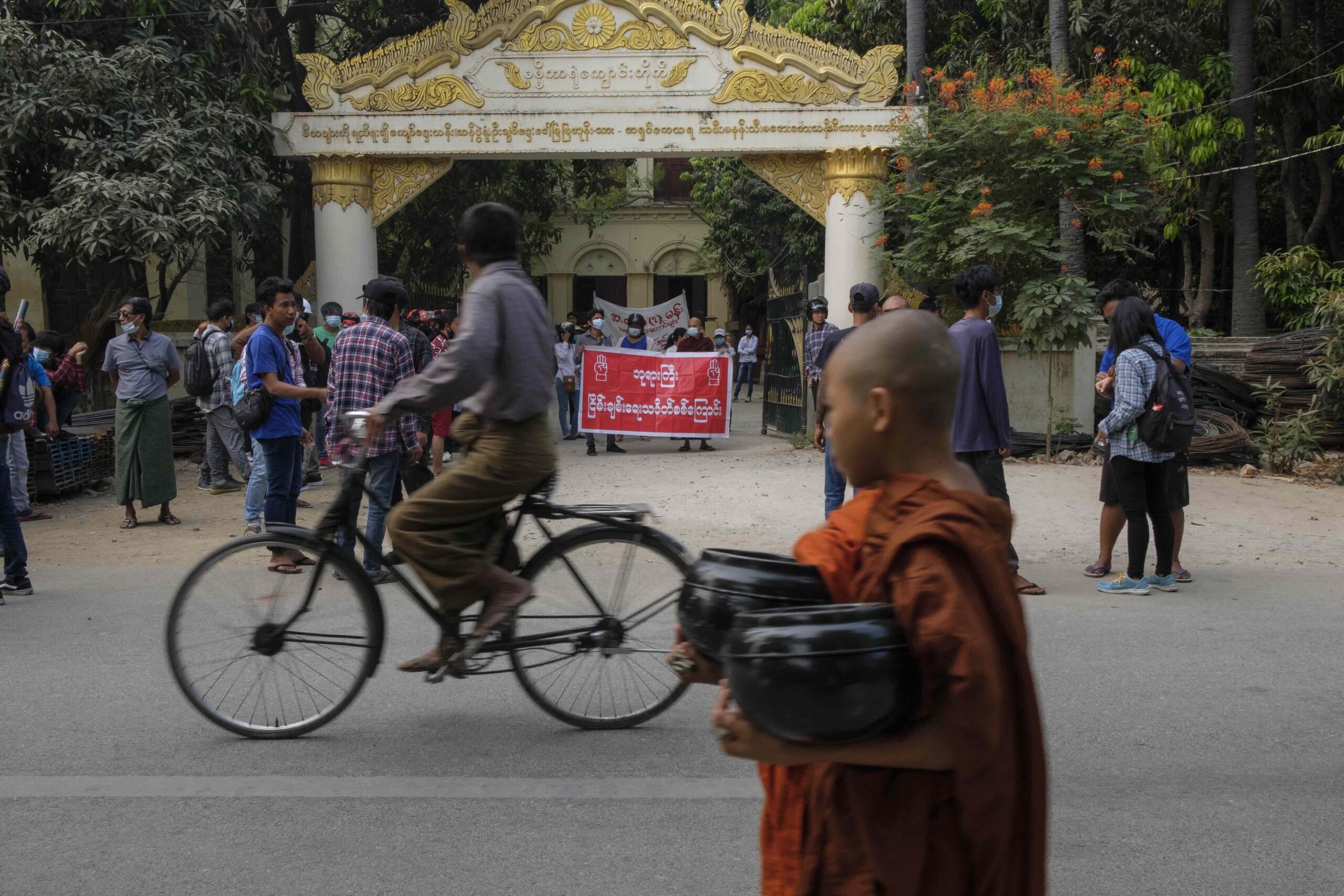 ၂၀၂၁ ခုနှစ် ဧပြီလ ၆ ရက်နေ့က မန္တလေးမြို့တွင် ဆန္ဒပြနေသူများအနီး ကိုရင်ငယ်တစ်ပါး ဖြတ်လျှောက်သွားစဉ်။ (ဓာတ်ပုံ-AFP)