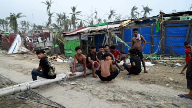 ၂၀၂၃ ခုနှစ် မေလ ၁၅ ရက်က မိုခါမုန်တိုင်းကြောင့် ပျက်စီးသွားသော စစ်တွေမြို့ အနောက်မြောက်ဘက် ခေါင်းဒုက္ကာရွာ (Khaung Dote Khar)ရှိ ဒုက္ခသည်စခန်းမှ အပျက်အစီးများ အနီး တွေ့ရသော ရိုဟင်ဂျာလူငယ်များ။ (ဓာတ်ပုံ-AFP)