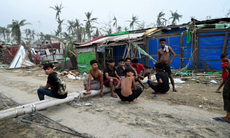 ၂၀၂၃ ခုနှစ် မေလ ၁၅ ရက်က မိုခါမုန်တိုင်းကြောင့် ပျက်စီးသွားသော စစ်တွေမြို့ အနောက်မြောက်ဘက် ခေါင်းဒုက္ကာရွာ (Khaung Dote Khar)ရှိ ဒုက္ခသည်စခန်းမှ အပျက်အစီးများ အနီး တွေ့ရသော ရိုဟင်ဂျာလူငယ်များ။ (ဓာတ်ပုံ-AFP)
