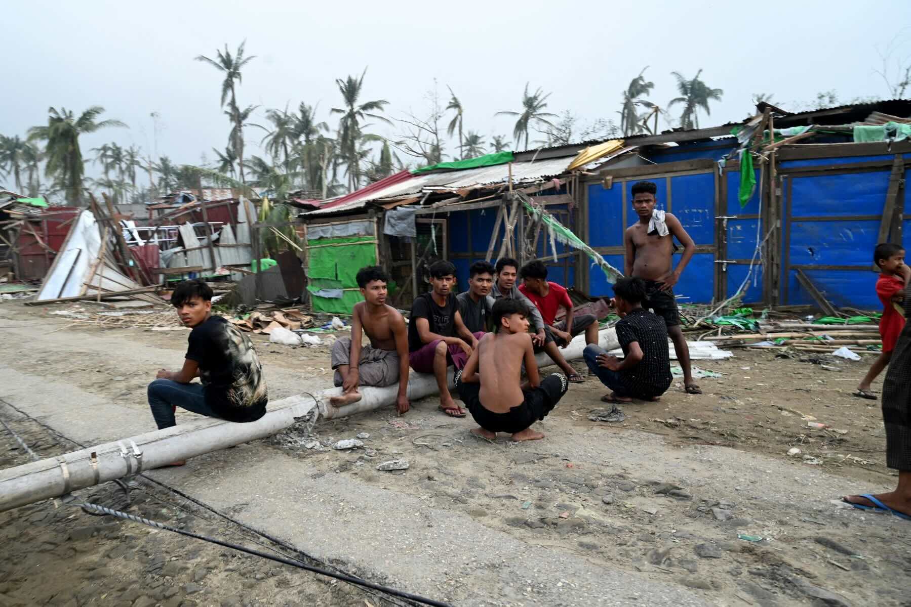 ၂၀၂၃ ခုနှစ် မေလ ၁၅ ရက်က မိုခါမုန်တိုင်းကြောင့် ပျက်စီးသွားသော စစ်တွေမြို့ အနောက်မြောက်ဘက် ခေါင်းဒုက္ကာရွာ (Khaung Dote Khar)ရှိ ဒုက္ခသည်စခန်းမှ အပျက်အစီးများ အနီး တွေ့ရသော ရိုဟင်ဂျာလူငယ်များ။ (ဓာတ်ပုံ-AFP)